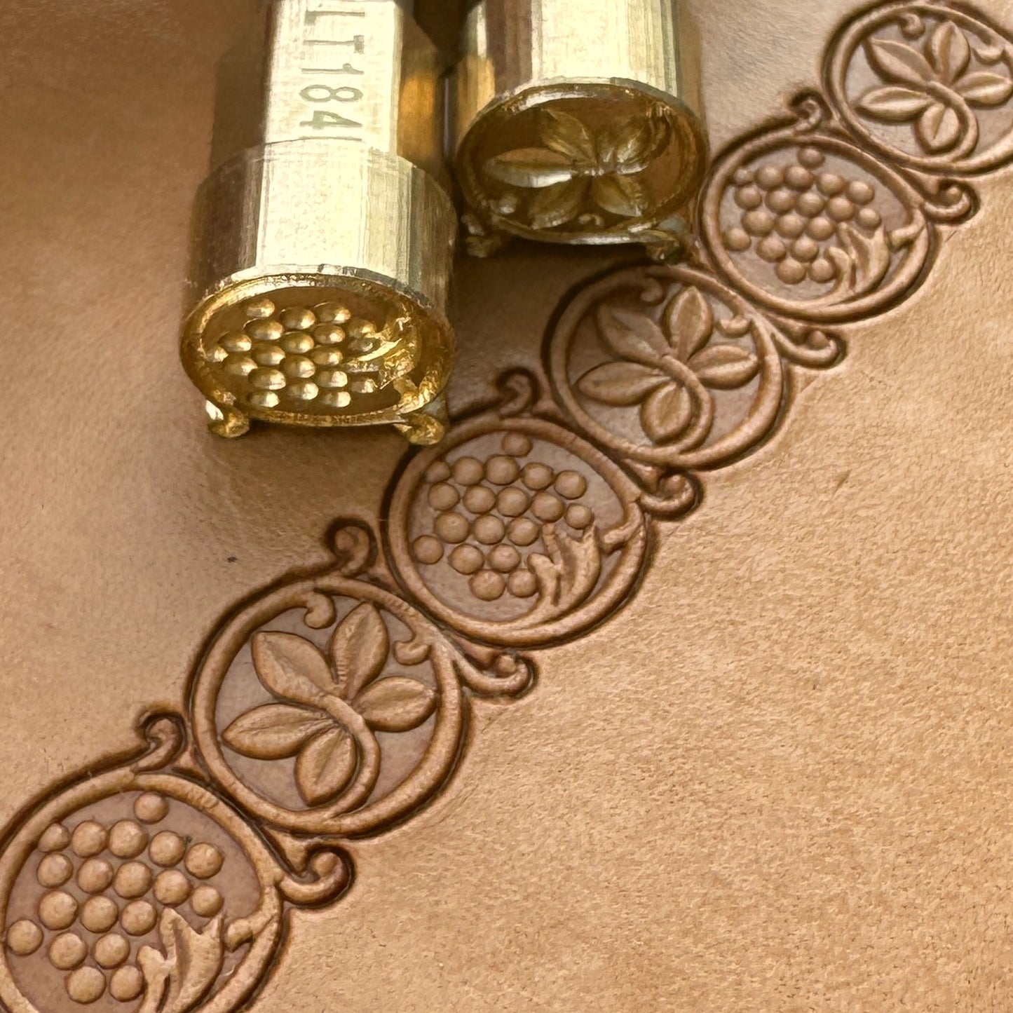 Grape Vine leather stamp LT184AB — hero shot of the two brass stamps with grape and leaf border impressions on veg-tan leather