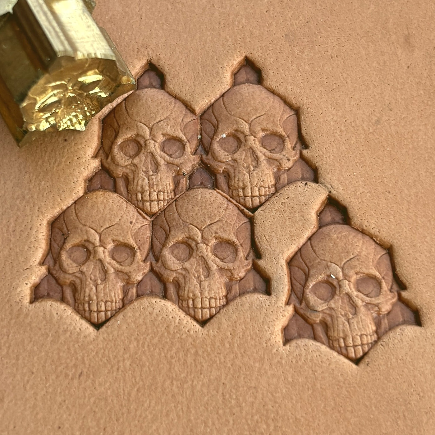 A cluster of skulls carved in deep relief into tan leather, with the brass stamp resting alongside.